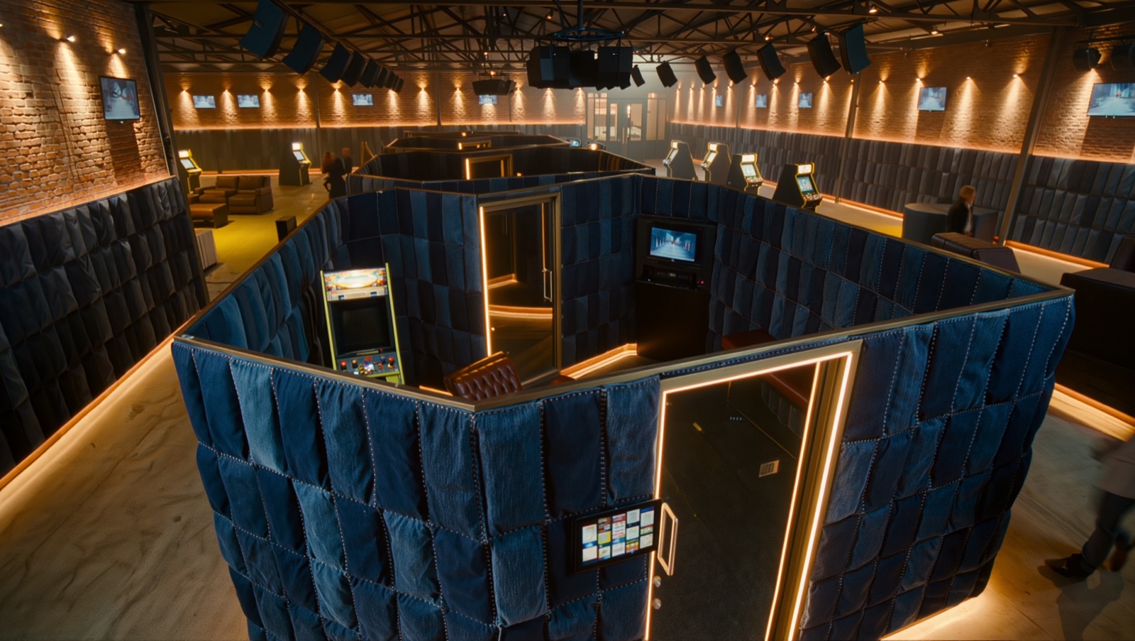 Concept render — a denim-clad sound booth: quilted indigo acoustic panels, amber halo, its own TV and arcade machine inside