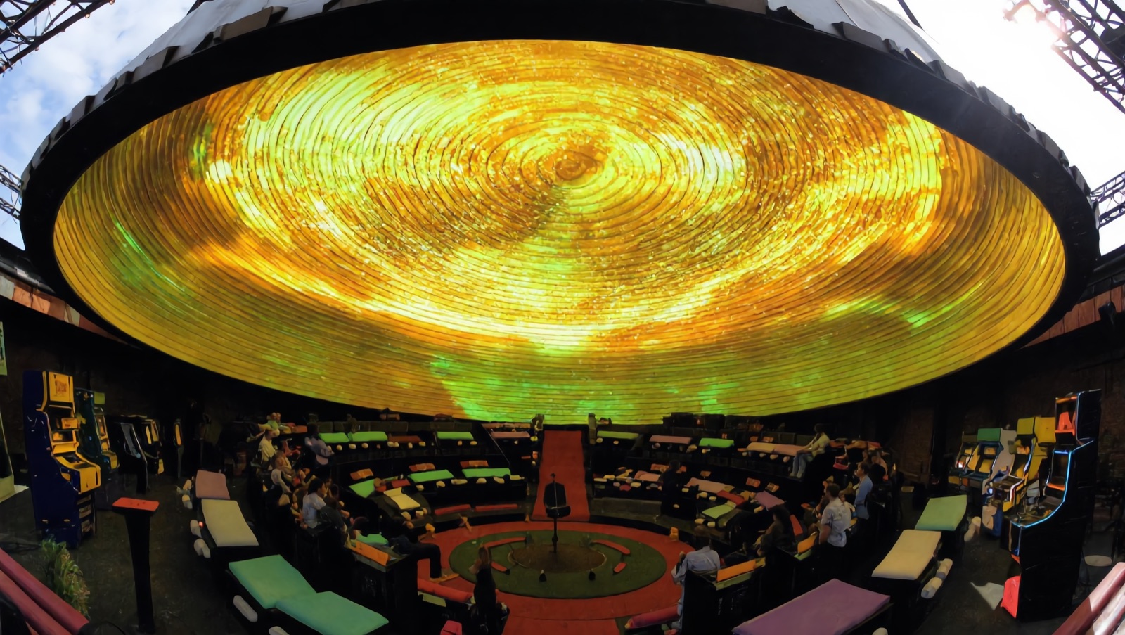 Concept render — the dome: a giant oval immersive screen crowning the spiral, the whole room looking up into one shared sky over the center stage